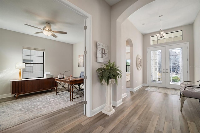 entrance foyer with arched walkways, ceiling fan with notable chandelier, wood finished floors, baseboards, and french doors