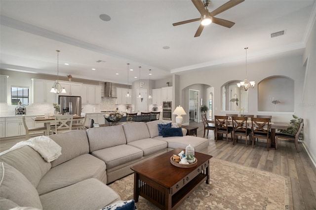 living room featuring visible vents, wood finished floors, ceiling fan with notable chandelier, crown molding, and recessed lighting