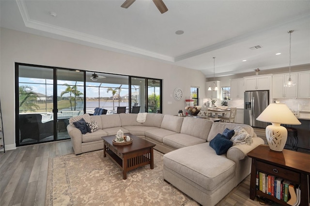 living room featuring visible vents, a raised ceiling, a ceiling fan, a water view, and light wood-style floors