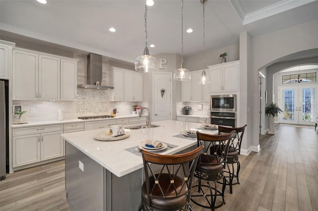 kitchen with arched walkways, wall chimney range hood, a sink, and white cabinets