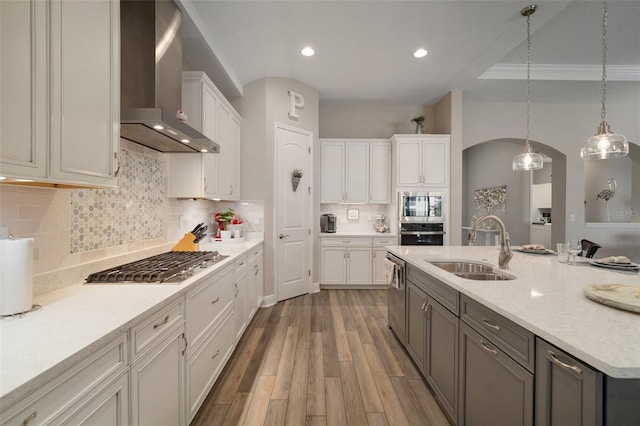 kitchen featuring white cabinets, wall chimney exhaust hood, stainless steel appliances, pendant lighting, and a sink