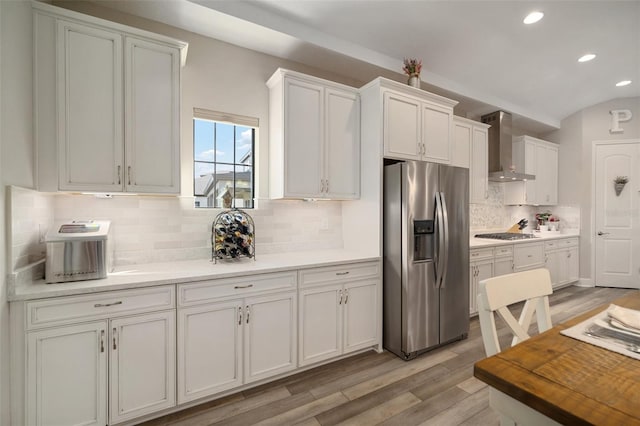 kitchen with white cabinets, stainless steel appliances, light countertops, light wood-type flooring, and wall chimney range hood