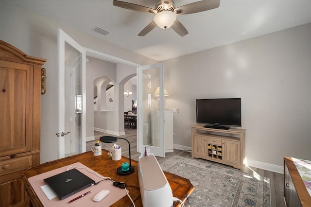 office area with arched walkways, light wood-style flooring, visible vents, baseboards, and a ceiling fan