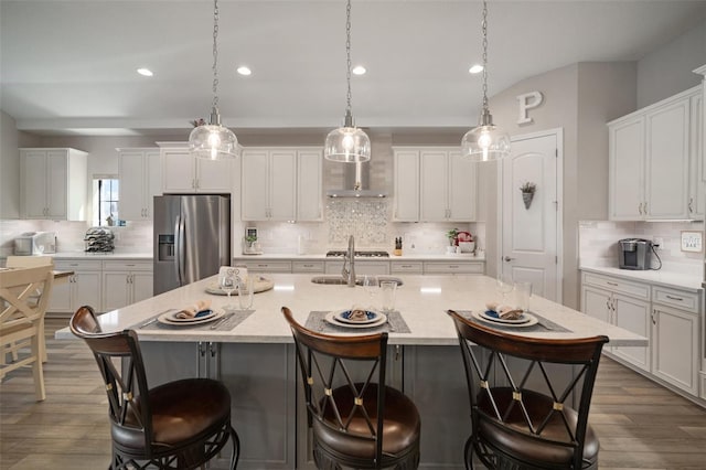 kitchen featuring white cabinets, an island with sink, decorative light fixtures, stainless steel appliances, and a kitchen bar