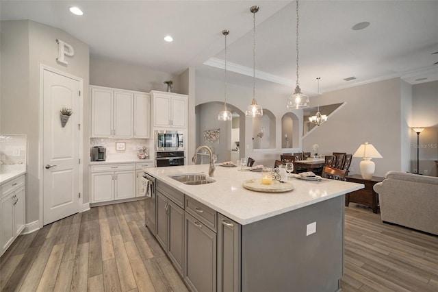 kitchen featuring stainless steel appliances, a sink, white cabinetry, open floor plan, and a center island with sink