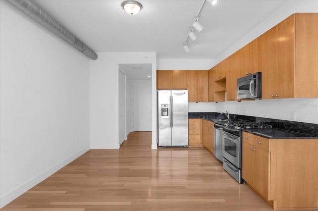 kitchen featuring sink, dark stone countertops, track lighting, appliances with stainless steel finishes, and light wood-type flooring