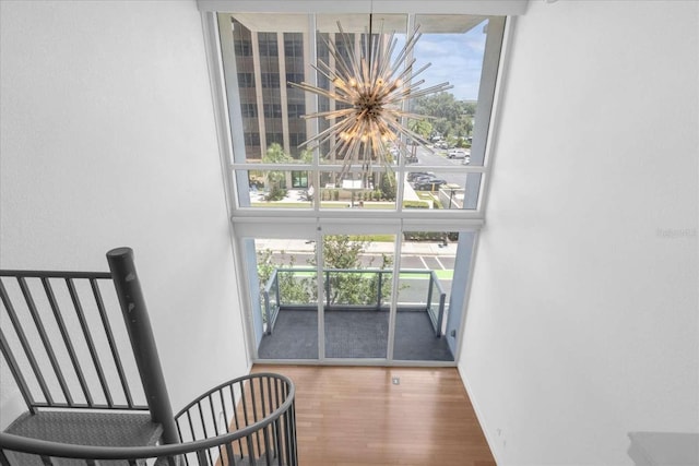interior space with a wall of windows, a chandelier, wood finished floors, plenty of natural light, and a towering ceiling