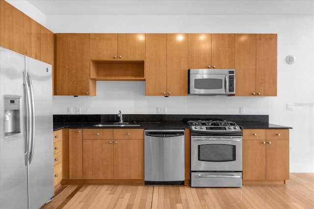kitchen with stainless steel appliances, a sink, light wood-type flooring, and dark stone counters