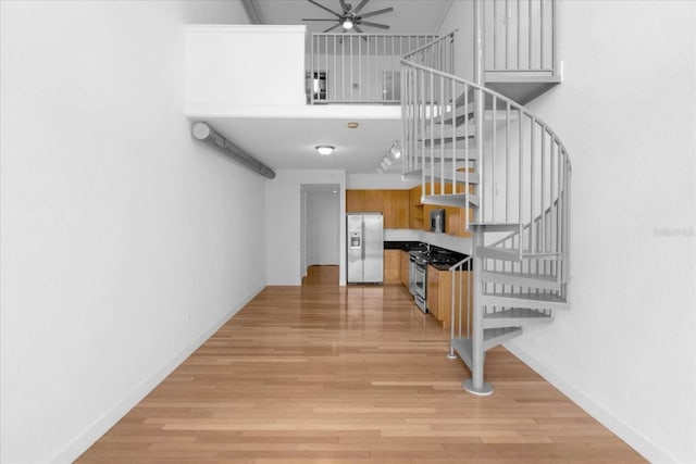 staircase with ceiling fan, wood finished floors, and baseboards