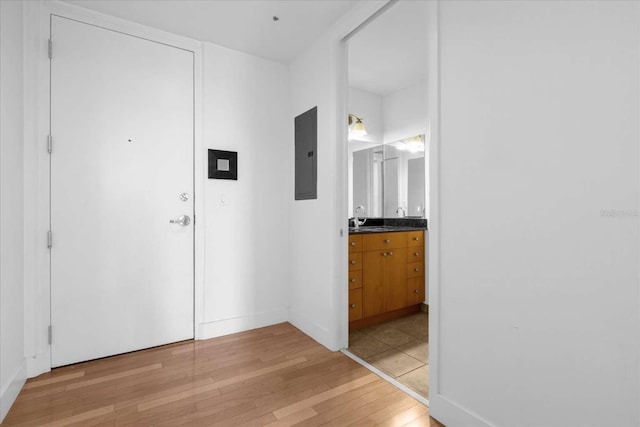 hallway with light wood-style flooring, electric panel, a sink, and baseboards