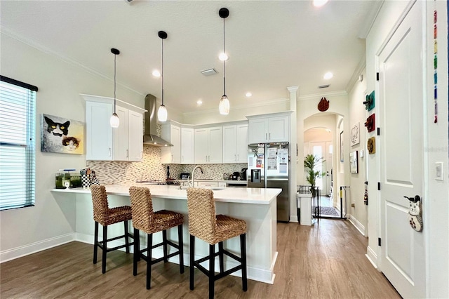 kitchen featuring white cabinetry, sink, hanging light fixtures, wall chimney range hood, and stainless steel refrigerator with ice dispenser