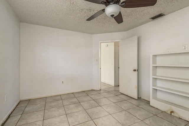 empty room with built in features, light tile patterned floors, and a textured ceiling