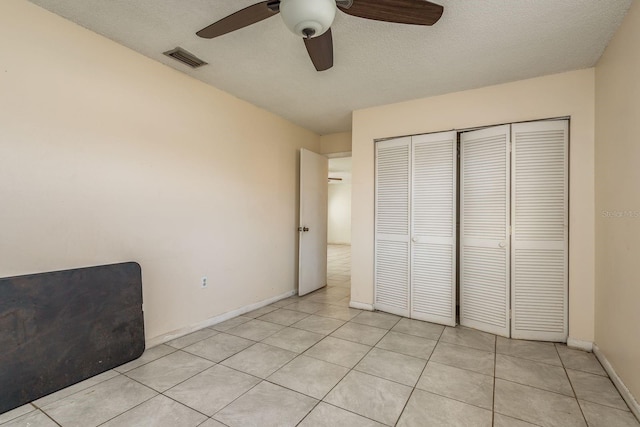 unfurnished bedroom with ceiling fan, a closet, light tile patterned flooring, and a textured ceiling