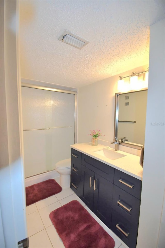 bathroom featuring tile patterned floors, vanity, a textured ceiling, toilet, and a shower with shower door