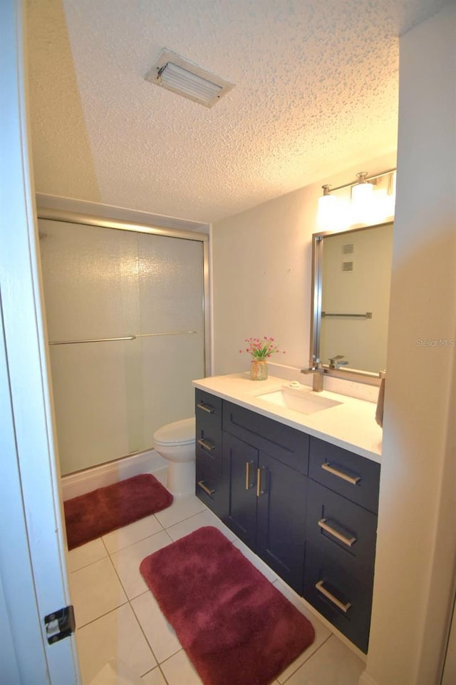 bathroom with vanity, a shower with door, tile patterned flooring, toilet, and a textured ceiling