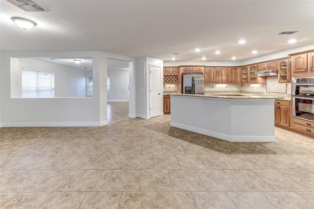 kitchen featuring a center island, backsplash, light stone countertops, light tile patterned floors, and stainless steel appliances