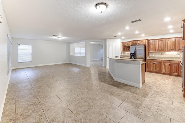 kitchen featuring light stone countertops, tasteful backsplash, stainless steel fridge, an island with sink, and a textured ceiling