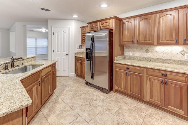 kitchen featuring light stone counters, sink, stainless steel refrigerator with ice dispenser, and tasteful backsplash