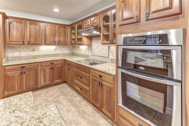 kitchen with black electric stovetop, light stone counters, stainless steel double oven, and tasteful backsplash