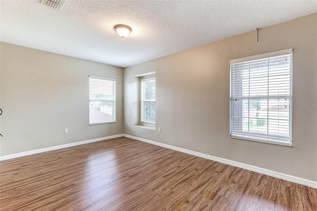 spare room featuring a textured ceiling, hardwood / wood-style flooring, and a healthy amount of sunlight