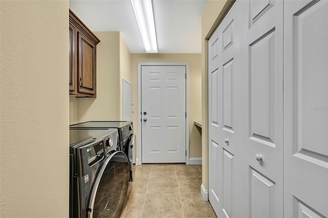 laundry area with washing machine and clothes dryer, light tile patterned flooring, and cabinets