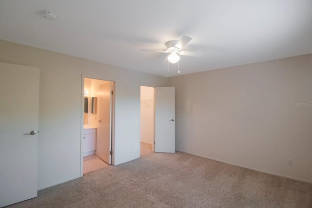 unfurnished bedroom with a walk in closet, ensuite bath, light colored carpet, ceiling fan, and a closet