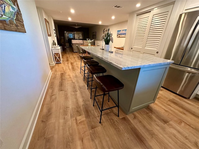 kitchen with light stone countertops, a center island, light hardwood / wood-style floors, and stainless steel refrigerator