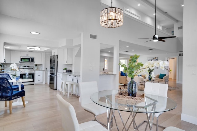 dining room with light hardwood / wood-style flooring, ceiling fan with notable chandelier, and a high ceiling