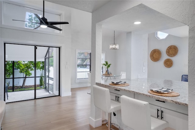 dining space with ceiling fan with notable chandelier, a high ceiling, a textured ceiling, and light hardwood / wood-style flooring