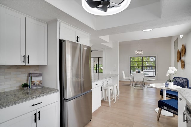 kitchen featuring white cabinets, stainless steel fridge, light hardwood / wood-style flooring, and light stone counters