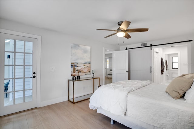 bedroom featuring access to exterior, ceiling fan, a barn door, multiple windows, and light hardwood / wood-style floors