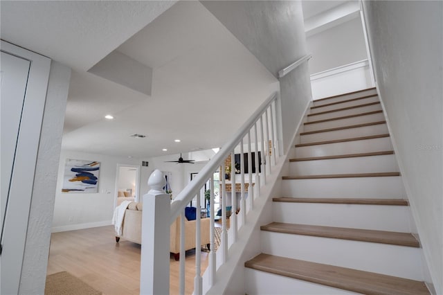 staircase with hardwood / wood-style floors and ceiling fan