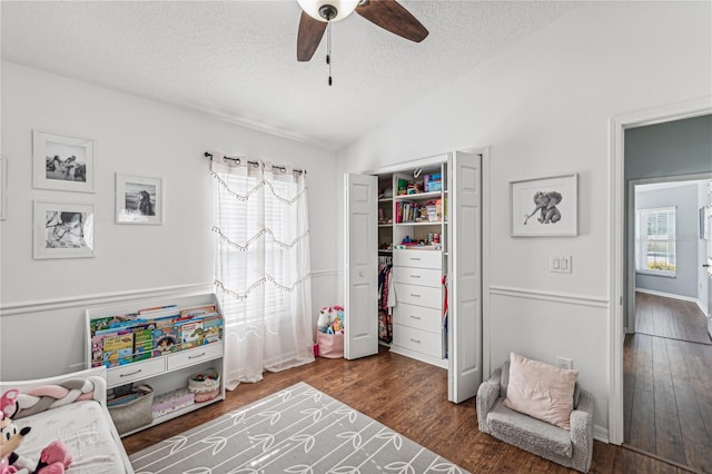 recreation room with a textured ceiling, vaulted ceiling, ceiling fan, and dark wood-type flooring