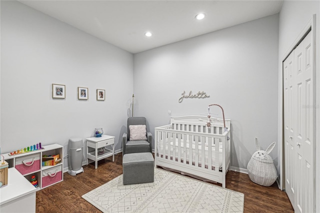 bedroom with a nursery area, dark hardwood / wood-style flooring, and a closet