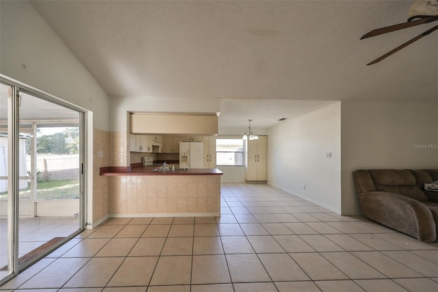 kitchen featuring kitchen peninsula, ceiling fan with notable chandelier, vaulted ceiling, white refrigerator with ice dispenser, and light tile patterned flooring