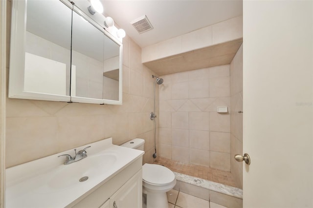 bathroom featuring tile patterned flooring, tiled shower, toilet, vanity, and tile walls