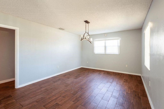 empty room featuring a notable chandelier, dark hardwood / wood-style floors, and a textured ceiling