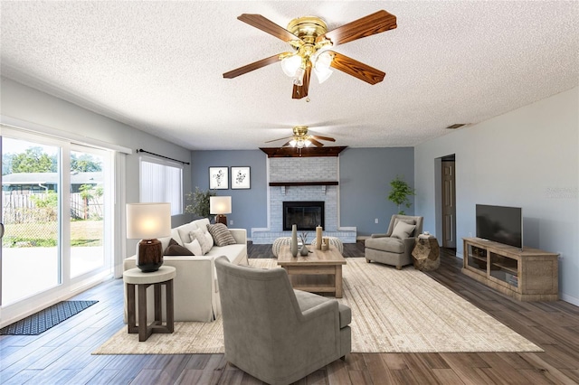 living room with ceiling fan, wood-type flooring, a textured ceiling, and a brick fireplace