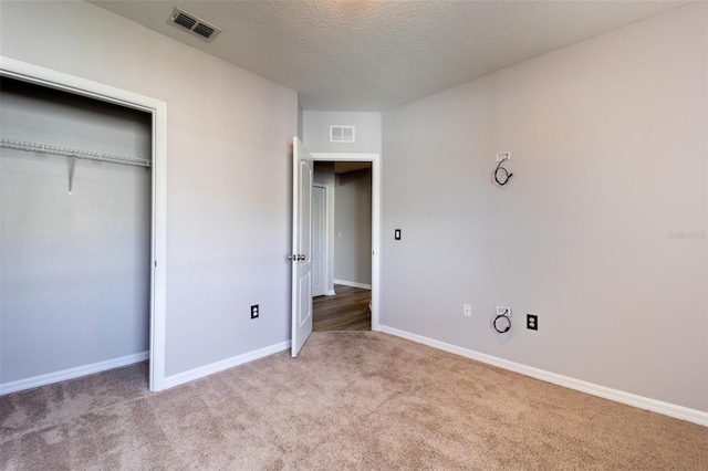 unfurnished bedroom with light colored carpet, a textured ceiling, and a closet