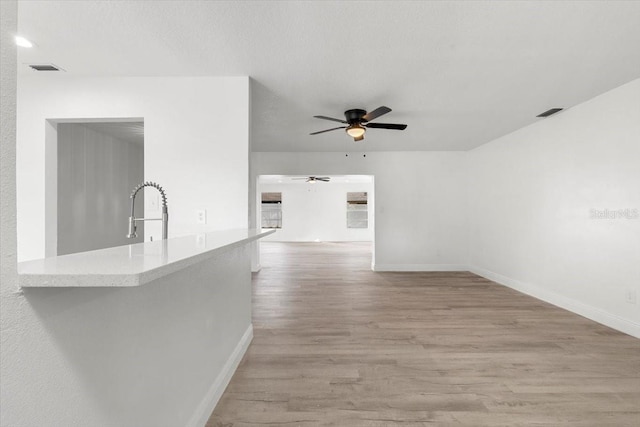 unfurnished living room with sink, a textured ceiling, light hardwood / wood-style floors, and ceiling fan