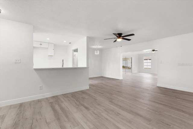 unfurnished living room featuring ceiling fan, sink, a textured ceiling, and light wood-type flooring