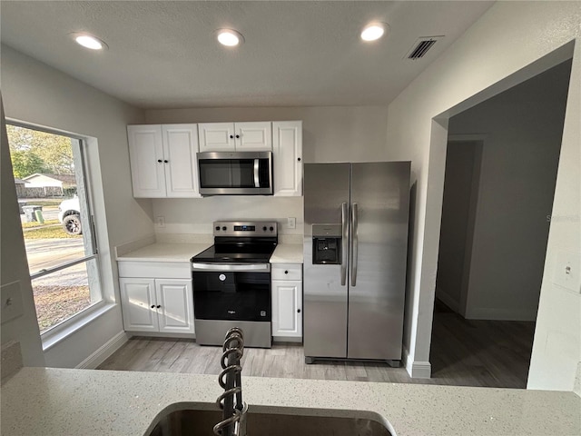 kitchen with sink, stainless steel appliances, white cabinets, and light wood-type flooring