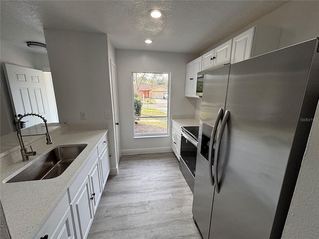 kitchen featuring sink, appliances with stainless steel finishes, white cabinetry, a textured ceiling, and light wood-type flooring