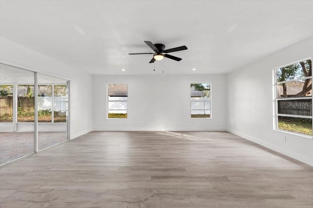 empty room featuring plenty of natural light, ceiling fan, and light wood-type flooring