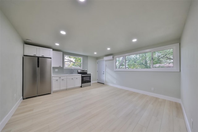 kitchen with a wall mounted air conditioner, sink, appliances with stainless steel finishes, light hardwood / wood-style floors, and white cabinetry