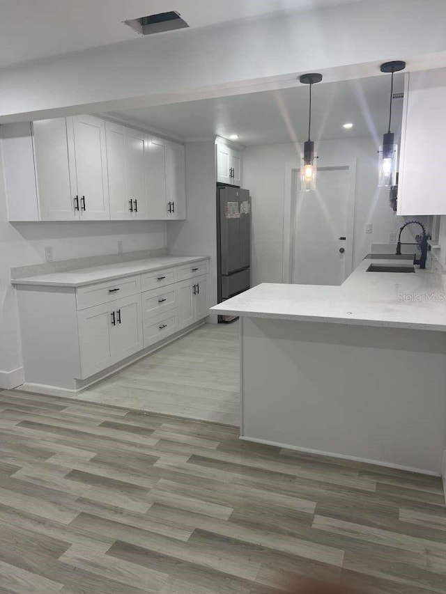 kitchen featuring sink, hanging light fixtures, light hardwood / wood-style flooring, fridge, and white cabinetry