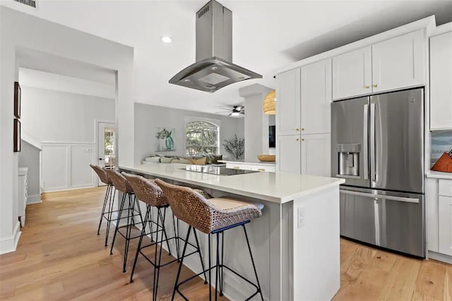 kitchen with stainless steel refrigerator with ice dispenser, a breakfast bar, island range hood, black electric cooktop, and white cabinetry