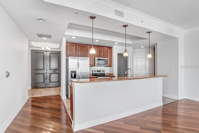 kitchen with pendant lighting, dark wood-type flooring, a textured ceiling, appliances with stainless steel finishes, and light stone counters