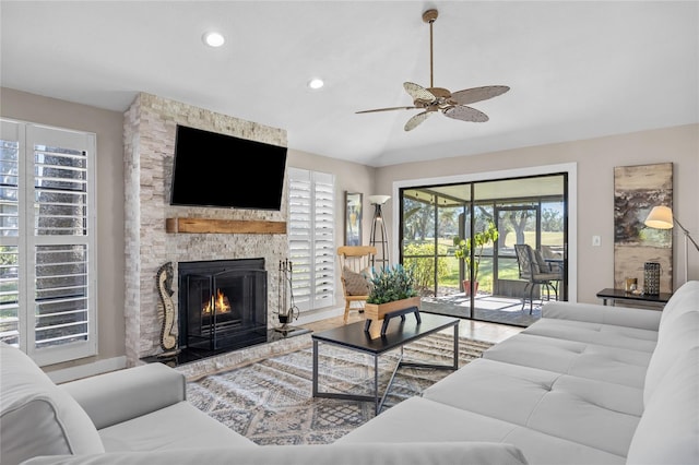 living room with ceiling fan, a stone fireplace, and vaulted ceiling