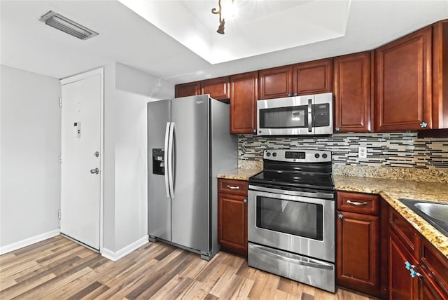 kitchen with decorative backsplash, a tray ceiling, light hardwood / wood-style flooring, stainless steel appliances, and light stone counters